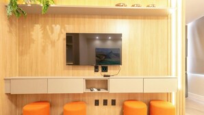 Un baño moderno con tocador de madera, televisor montado y taburetes naranja.