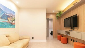 Una sala moderna con un sofá beige, un televisor de pantalla plana montado en una pared de madera y un cuadro con una escena costera.
