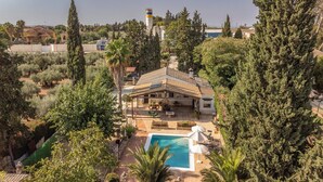 A villa with a swimming pool, surrounded by trees and a view of the sea.
