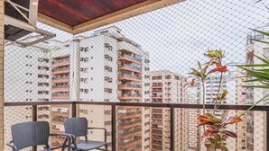 Un balcon avec deux chaises et une plante, donnant sur un immeuble de grande hauteur doté de nombreux balcons.