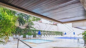 Un espace extérieur abrité avec une piscine, des chaises longues et un sol carrelé.