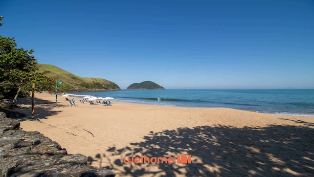 Una playa con cielo despejado, orilla arenosa y una pequeña isla a lo lejos.