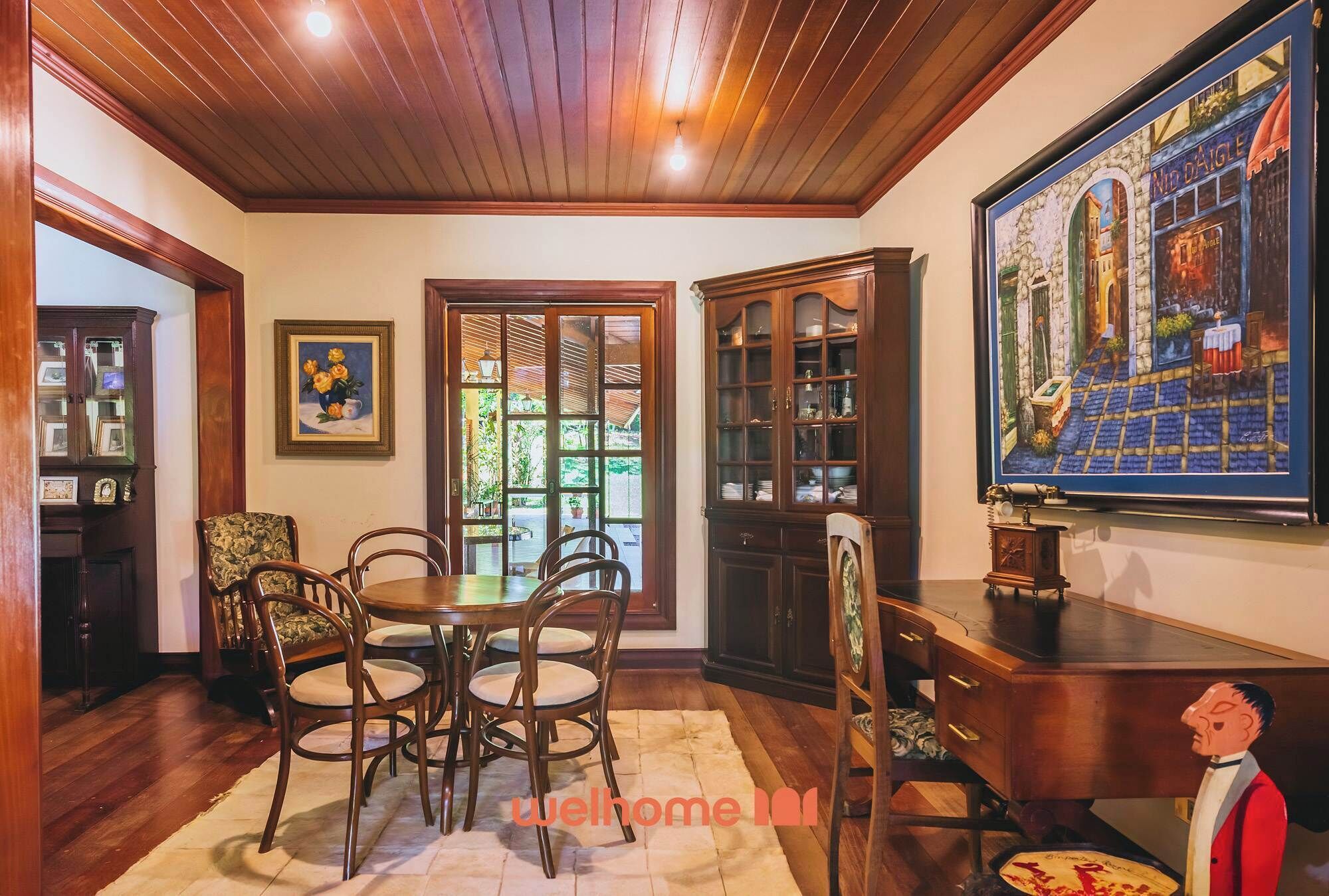 A dining area with wooden furniture, a large painting, and a view through a window.