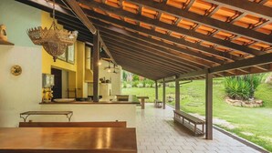 A covered outdoor dining area with a pergola, benches, and a view of a garden. - Sitio em Indaiatuba com Piscina e Churrasqueira (Campinas)