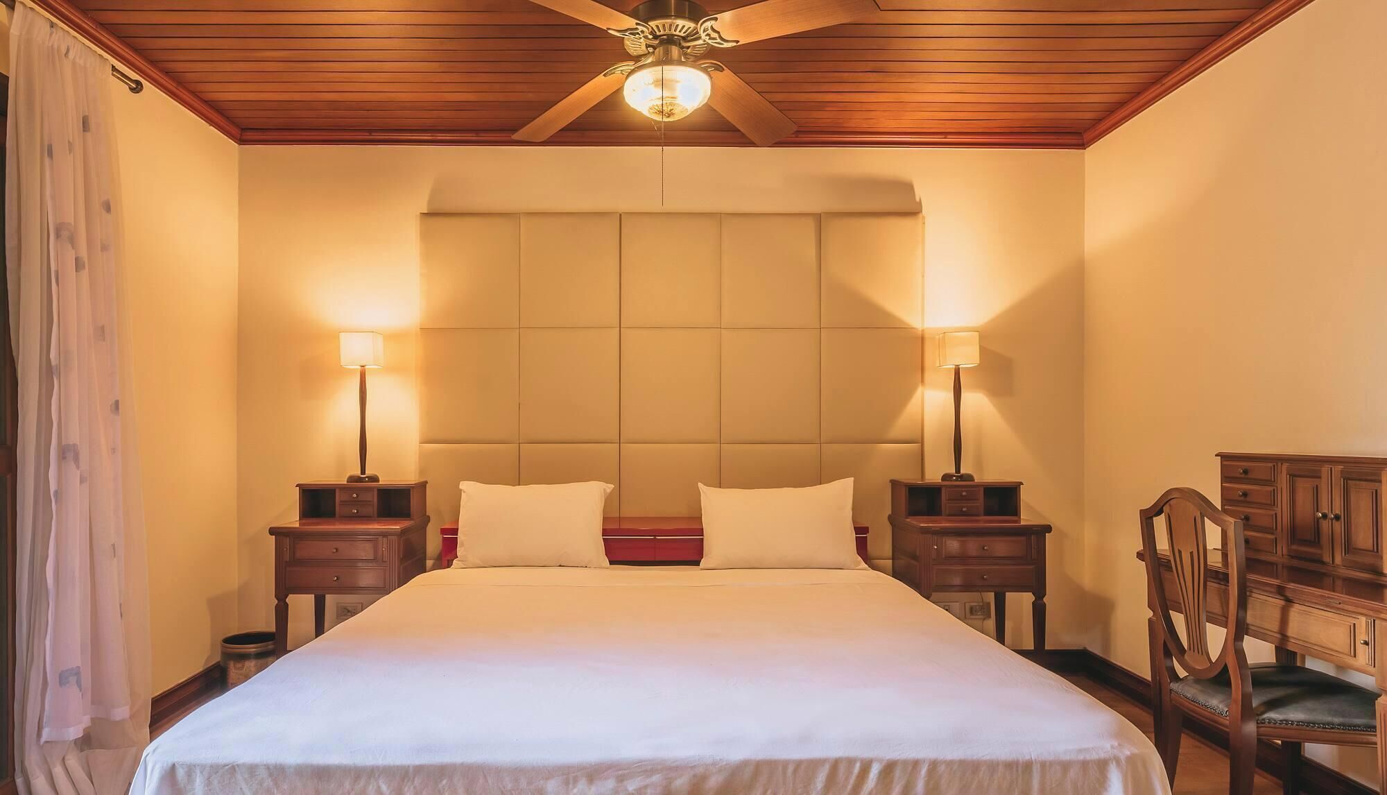 Een hotelkamer met een groot bed, twee nachtkastjes met lampen, een houten hoofdeinde en een plafondventilator.