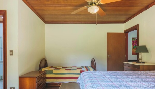 A bedroom with a wooden ceiling, a bed with a plaid bedspread, a nightstand with a lamp, a dresser, and a door with a painting. - Sitio em Indaiatuba com Piscina e Churrasqueira (Campinas)