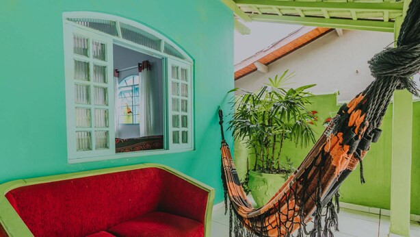 Una habitación con un sofá rojo, una hamaca y una ventana con contraventanas blancas.