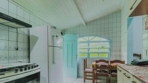 Una cocina con paredes de azulejos blancos, un refrigerador blanco, una estufa y un ventanal con marco azul.