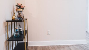 A room with a wooden floor, a black metal shelf with decorative items, and a plain wall. - Unparalleled Convenience | City View | Food Scene (Atlanta)