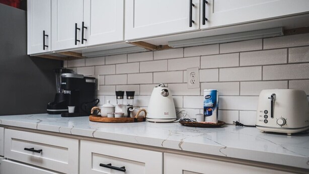 A kitchen with white cabinets, a coffee maker, a kettle, and a toaster on the counter. - Unparalleled Convenience | City View | Food Scene (Atlanta)