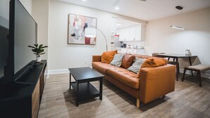 A modern living room with a leather sofa, a flat-screen TV, and a dining area with a table and chairs. - Unparalleled Convenience | City View | Food Scene (Atlanta)