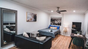 Ein gemütliches Schlafzimmer mit Bett, Sofa, kleinem Tisch, Fernseher und Deckenventilator.