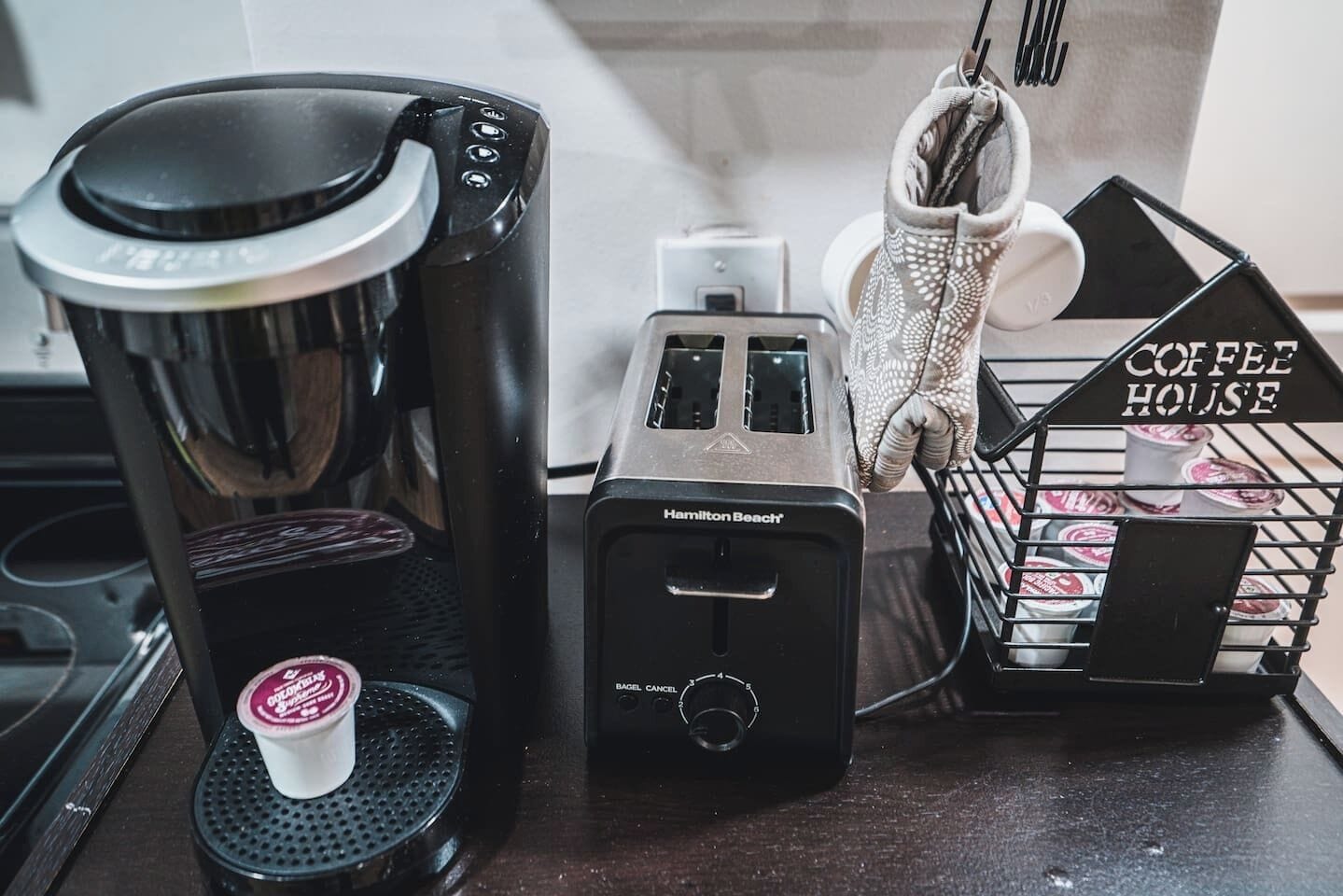 A coffee maker, a toaster, and a basket labeled "Coffee House" on a kitchen counter.