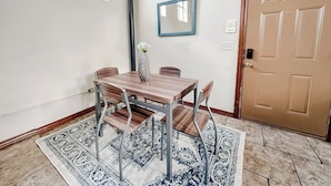 Ein Essbereich mit einem Holztisch und Stühlen, einer Blumenvase, einem gemusterten Teppich, einem Spiegel an der Wand und einer Tür mit Griff.