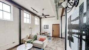 Ein geräumiges Wohnzimmer mit einer Couch, einem Couchtisch und Sesseln. Es gibt einen Deckenventilator, ein Bild an der Wand und eine Tür im Hintergrund.