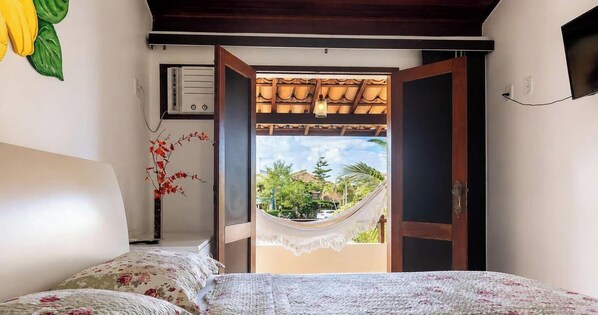 A bedroom with a bed, a bedside table with a vase, a view of a hammock outside, and a door leading to an outdoor area.