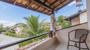 Een balkon met een houten stoel, een hanglamp en uitzicht op palmbomen en huizen.