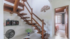 Een modern interieur met een houten spiraaltrap, een decoratieve wanddecoratie van een boom, een kleine potplant en een ventilator.