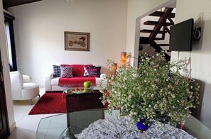 Uma sala de estar moderna com um sofá vermelho, poltronas brancas, uma mesa de centro com frutas e um grande arranjo floral.