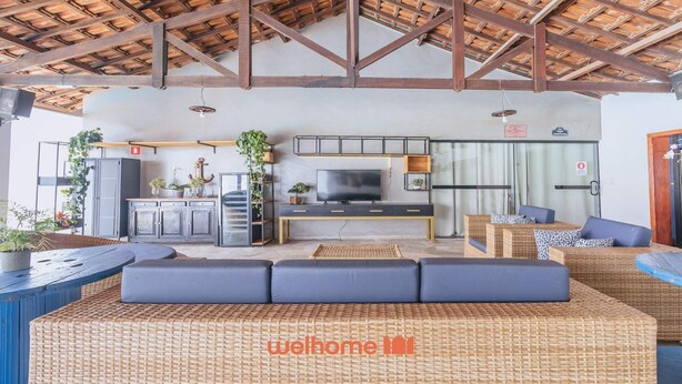 Una sala de estar moderna con un sofá grande, una televisión y una zona de cocina con armarios y plantas.