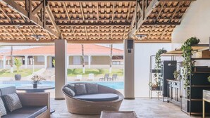Un espacio de estar al aire libre techado, con vista a la piscina, mobiliario de mimbre y una moderna zona de cocina.