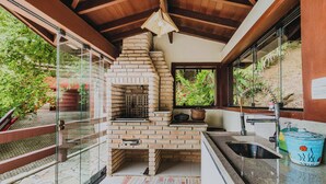 A kitchen with a brick oven, a sink, and a window overlooking greenery. - Casa em São Sebastião com Piscina, Jacuzzi e Vista (São Sebastião)