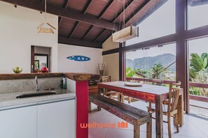 Eine Küche mit Holztisch und Bank, einem Spülbecken und Blick auf Berge durch große Fenster.