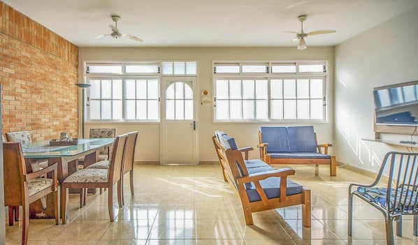 Un amplio salón con una pared de ladrillo decorativa, una mesa de comedor con sillas, un sofá y un televisor fijado a la pared.