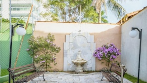Un patio con una fuente de piedra, dos bancos y un muro con un diseño decorativo.