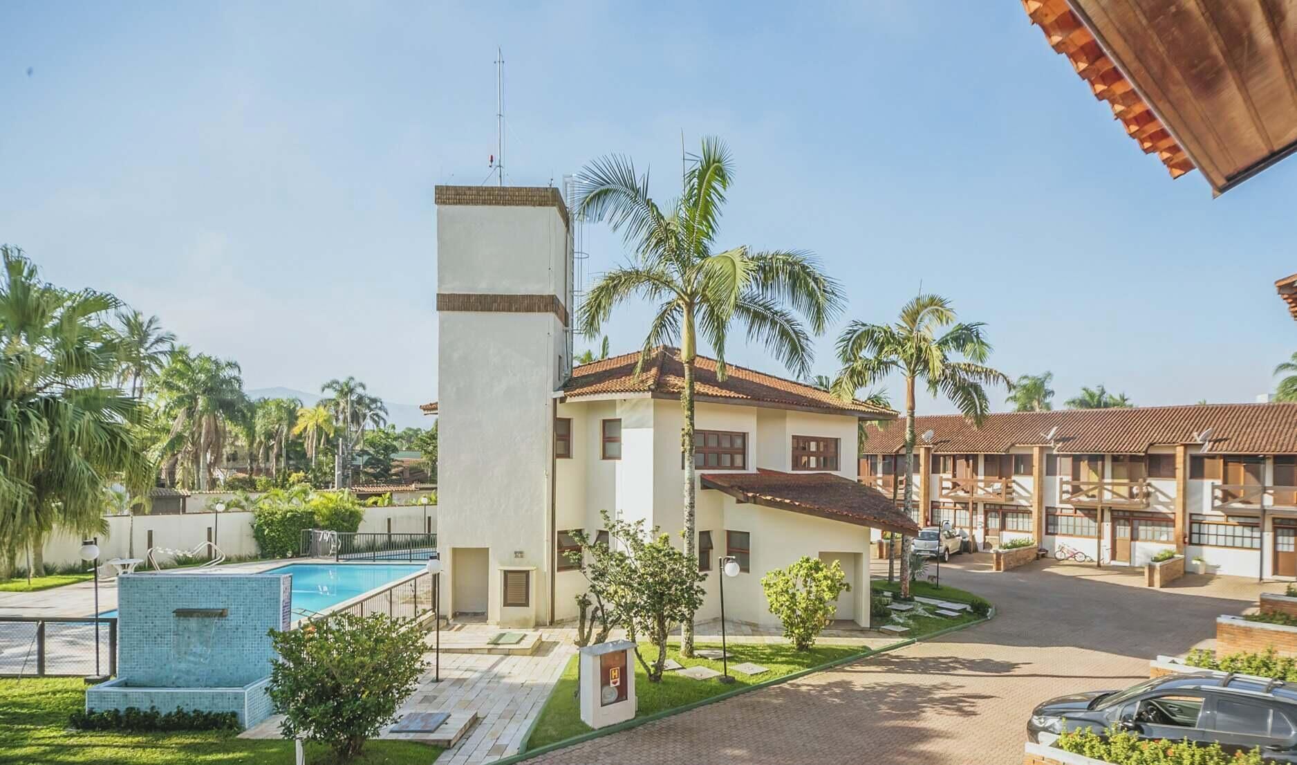 A resort with a swimming pool, palm trees, and a two-story building with a tiled roof.