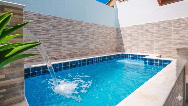 A swimming pool with a tiled edge, a water feature, and a palm tree. - Casa em Itanhaém com piscina 5 min de carro da Praia (Itanhaém)