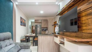 A modern kitchen with a large TV, wooden cabinets, and a dining area with a gray sofa. - Casa em Itanhaém com piscina 5 min de carro da Praia (Itanhaém)
