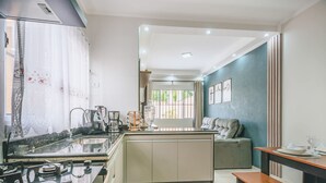 A modern kitchen with a central island, a dining area with a sofa, and a view through a window with metal bars. - Casa em Itanhaém com piscina 5 min de carro da Praia (Itanhaém)