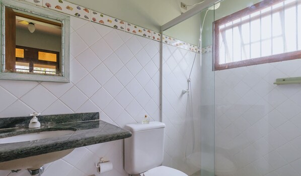 A bathroom with a white tiled wall, a marble countertop, a toilet, and a shower enclosure. - Casa em Ubatuba perto da Praia Lagoinha e Piscina (Lagoinha)
