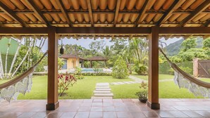 Ein überdachter Außenbereich mit Pool, Pavillon und Blick auf ein Haus im Hintergrund.