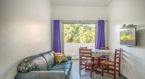 A room with a sofa, a dining table with chairs, a TV mounted on the wall, and a window with purple curtains.