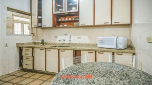 A kitchen with a granite countertop, white cabinets, a microwave, and a sink.