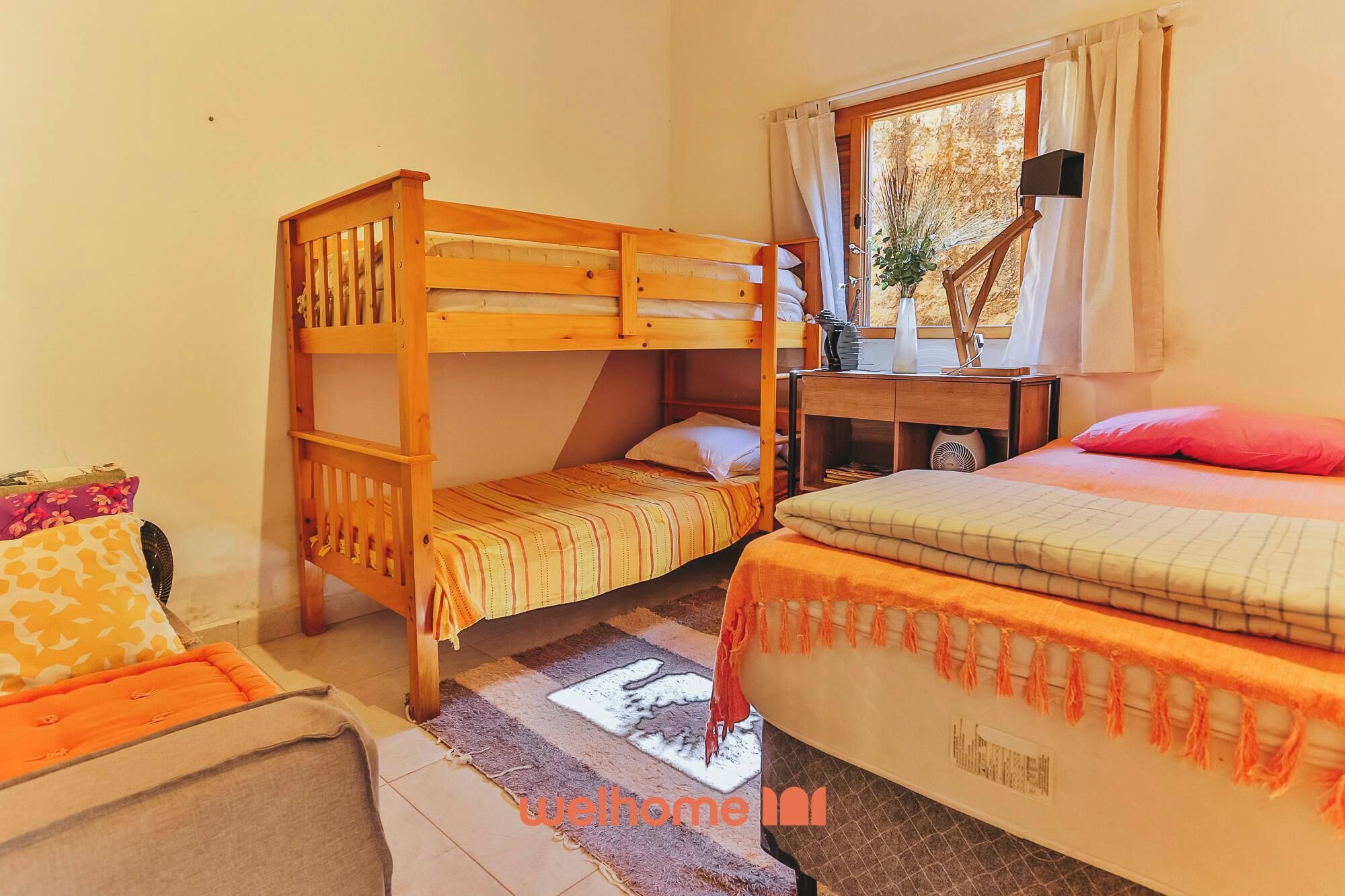 Una habitación con dos literas, una mesita con una lámpara, una ventana con cortinas y un radiador.