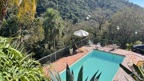 A pool area with a view of a forested hillside, surrounded by various plants and a metal railing. - Casa em Mairinque em meio a Natureza com Piscina (Mairinque)