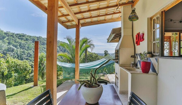 A covered outdoor area with a table and chairs, a hammock, and a view of a lush landscape.