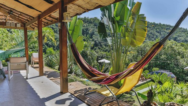 A hammock under a wooden pergola with a view of lush greenery and a car in the background. - Casa em Mairinque em meio a Natureza com Piscina (Mairinque)