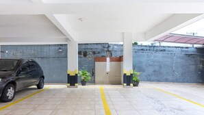 Un estacionamiento con un coche aparcado en el carril izquierdo. Hay líneas amarillas en el suelo, una pared de azulejos y una pared de hormigón con techo metálico al fondo.