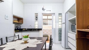 Una cocina compacta con armarios blancos, una encimera de madera y una mesa con un mantel individual de crochet.