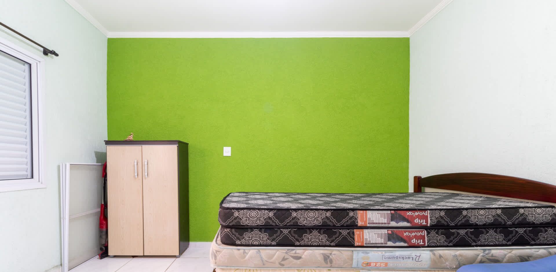 A small room with a green wall, a wooden wardrobe, and a bed with a patterned mattress.