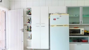A kitchen with white cabinets, a refrigerator, a microwave, and a glass cabinet. - Casa em Peruíbe com Piscina e Churrasqueira (Peru íbe)