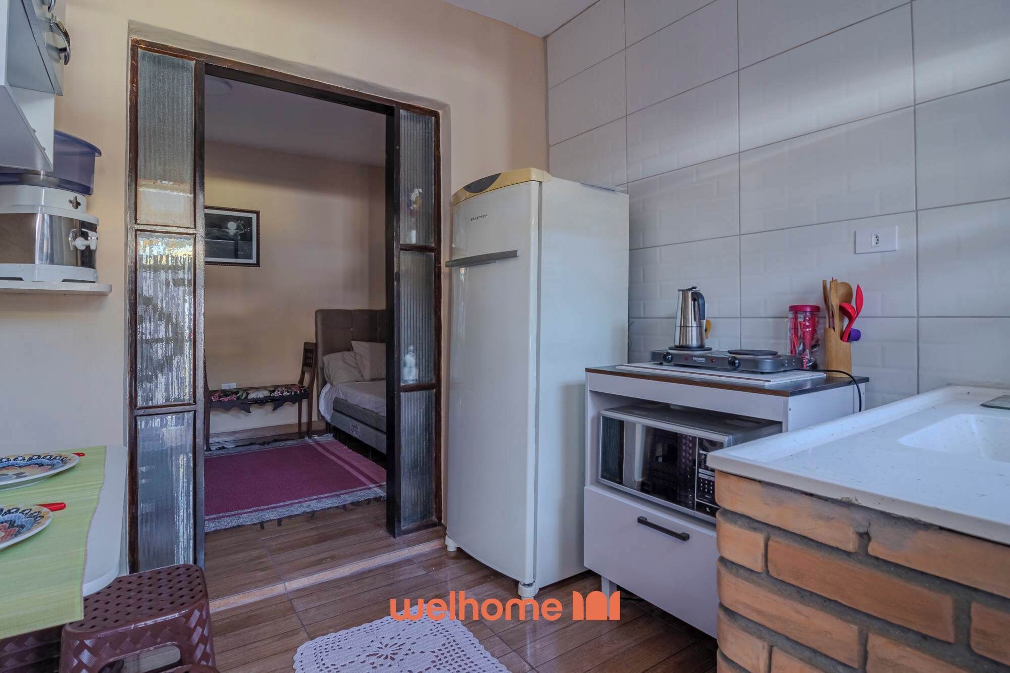 A compact kitchen with a refrigerator, stove, and sink. A dining area with a table and chairs is visible through an open door.