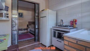 A compact kitchen with a refrigerator, stove, and sink. A dining area with a table and chairs is visible through an open door. - Casa em São Sebastião a 5 min da Praia (São Sebastião)