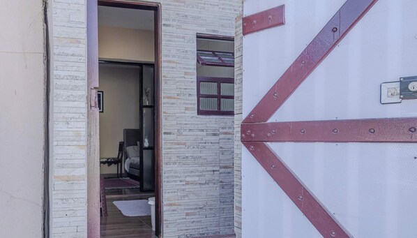 A doorway leading to a room with a bed, a small window, and a door with a metal handle. - Casa em São Sebastião a 5 min da Praia (São Sebastião)