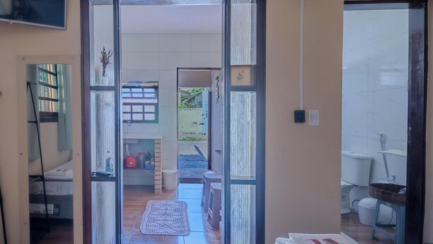 A room with a bed, a small table, and a window. There is a door leading to another room. - Casa em São Sebastião a 5 min da Praia (São Sebastião)