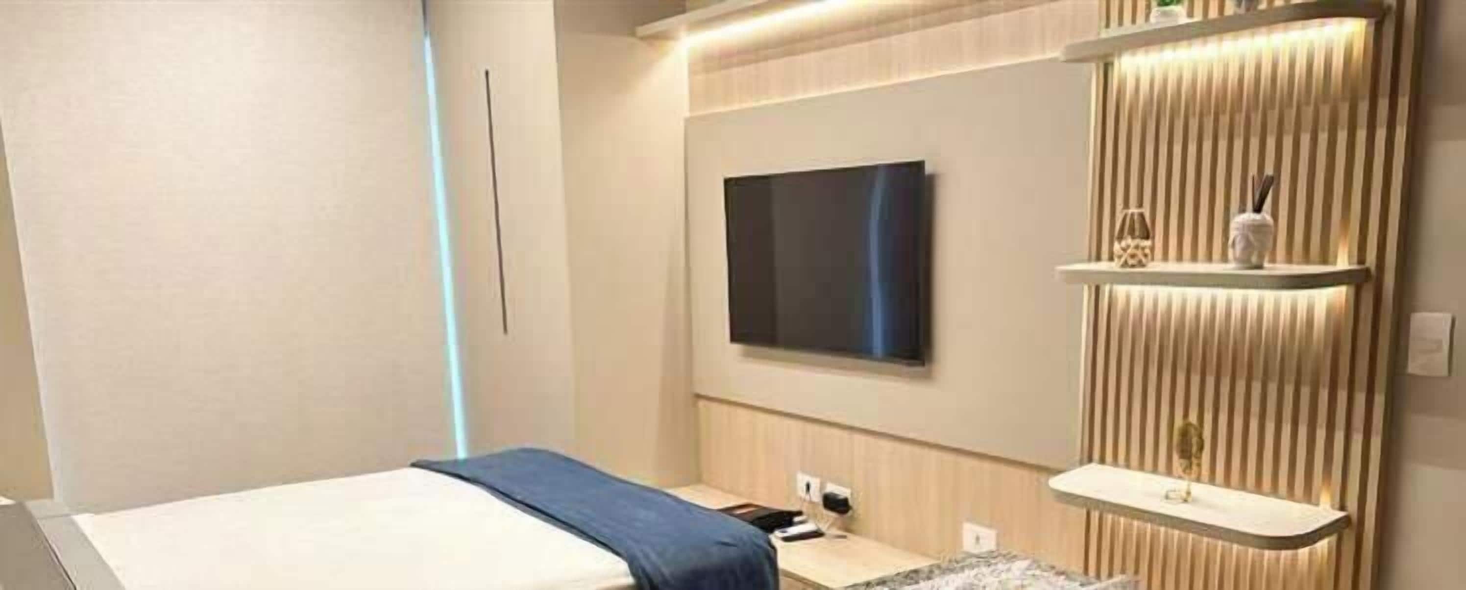 Moderni hotellihuone, jossa on sänky, seinälle asennettu taulutelevisio, yöpöytä ja hylly, jossa on koriste-esineitä.